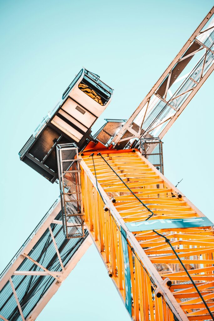 A striking low angle shot of a vibrant yellow tower crane against a clear sky, showcasing industrial power.